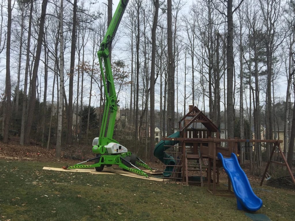 Green crane positioned near playground in wooded area