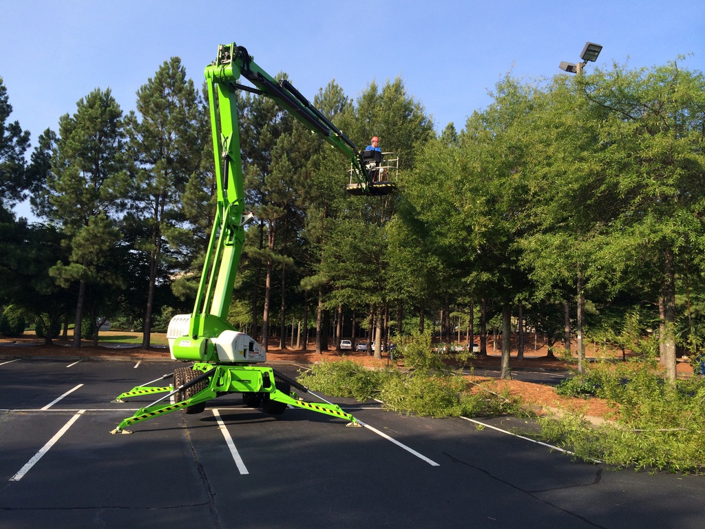 A green lift platform with an operator working in trees