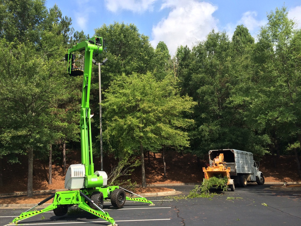 Green aerial lift in action near a tree chipper.